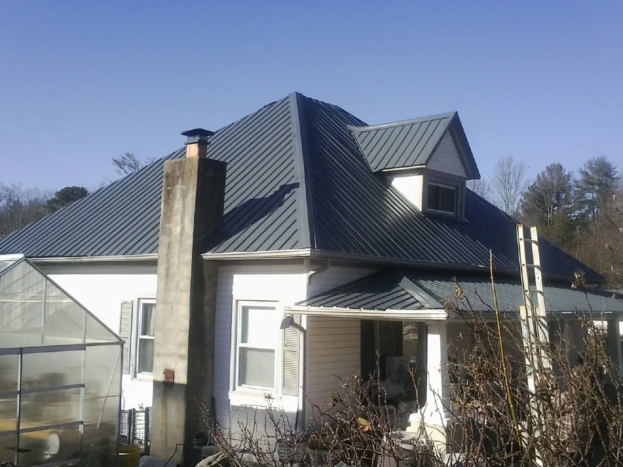 Dark blue standing seam metal roof on a white farmhouse with dormer — Slate & Tile Roof Repair by Roofing Brothers in Blue Diamond