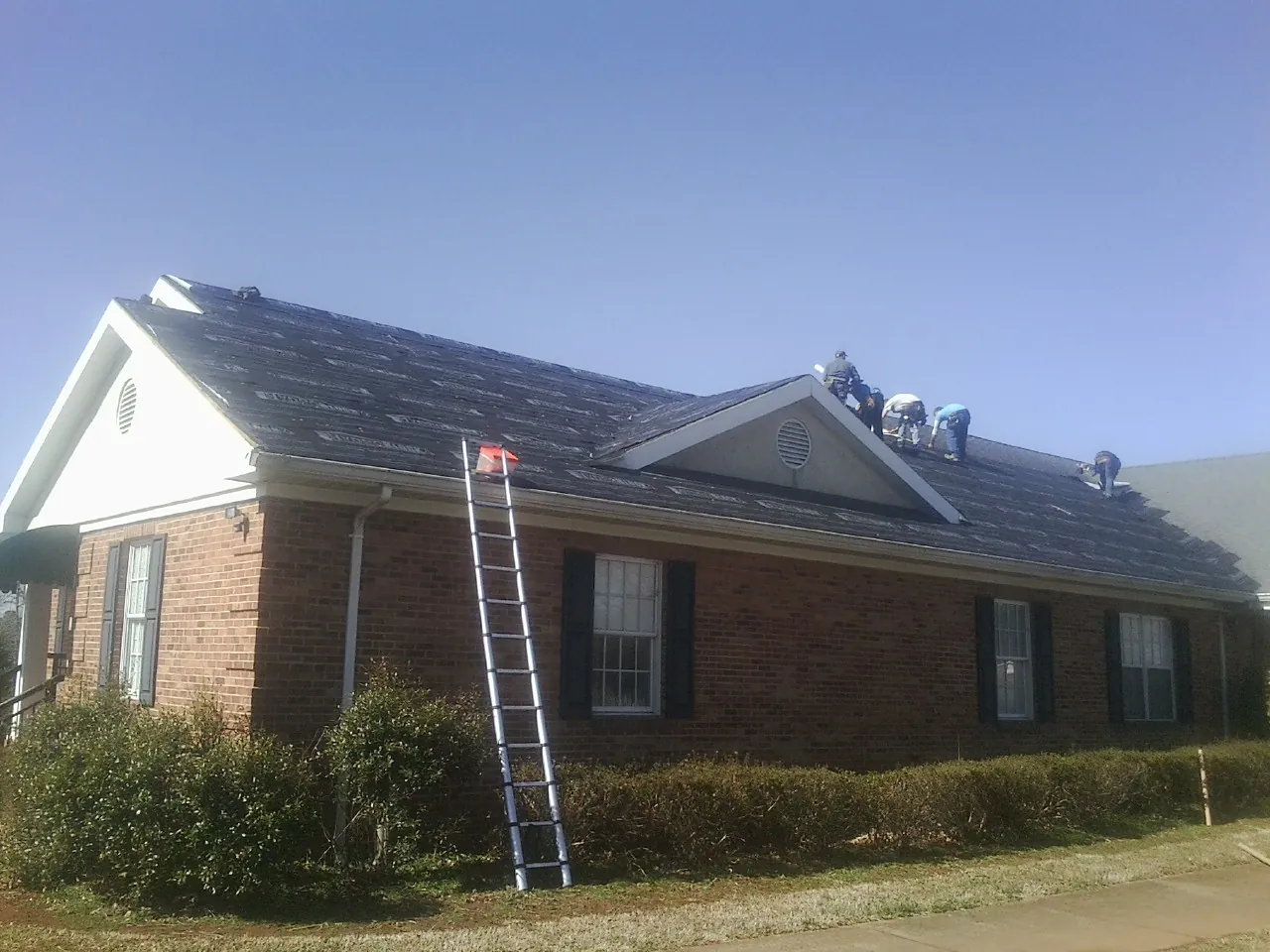 Crew tearing shingles off a brick ranch roof with a ladder set — Emergency Roof Repair work by our crew in Blue Diamond