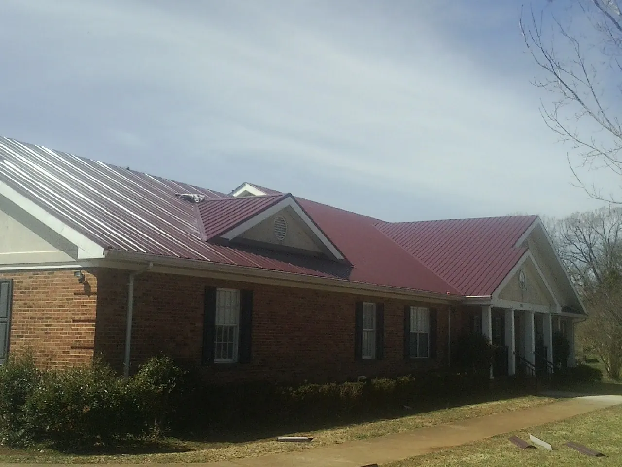 Red metal roof with gabled entries on a long brick building, from a Hail Damage Roof Repair job in Blue Diamond