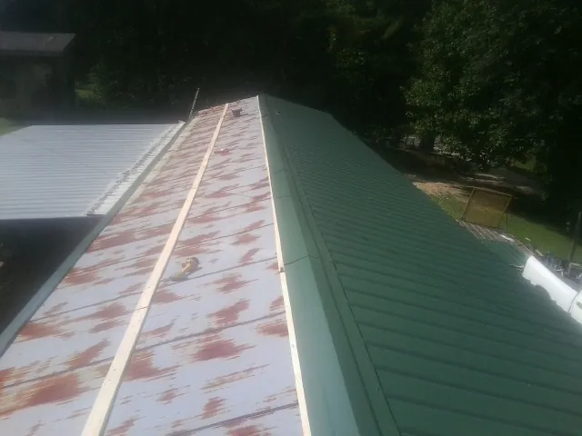 Old rusted panels beside newly installed green metal roofing — Wind Damage Roof Repair by Roofing Brothers in Blue Diamond