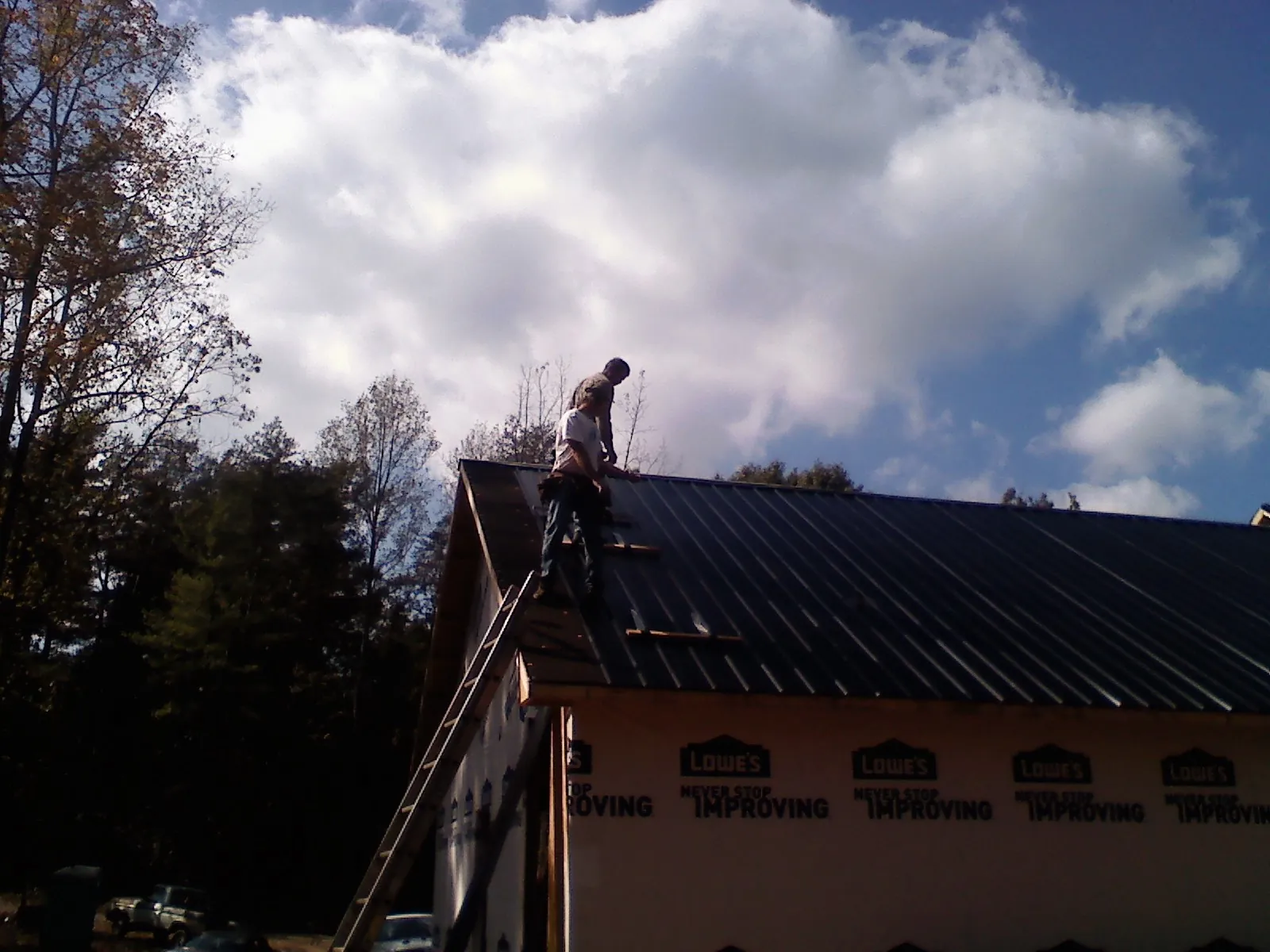 Roofer fastening dark metal panels high against a cloudy sky, from a Roof Inspection job in Blue Diamond