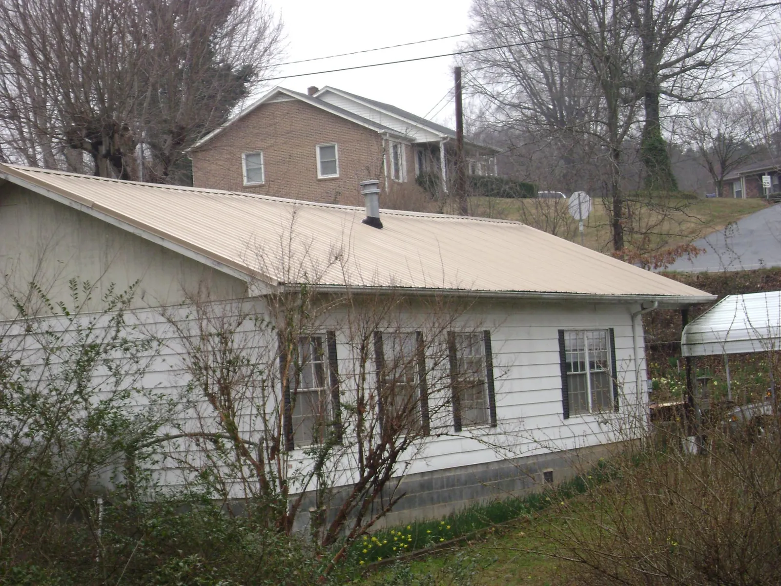 Tan metal roof on a white sided house set into a hillside — Commercial Roofing by Roofing Brothers in Blue Diamond